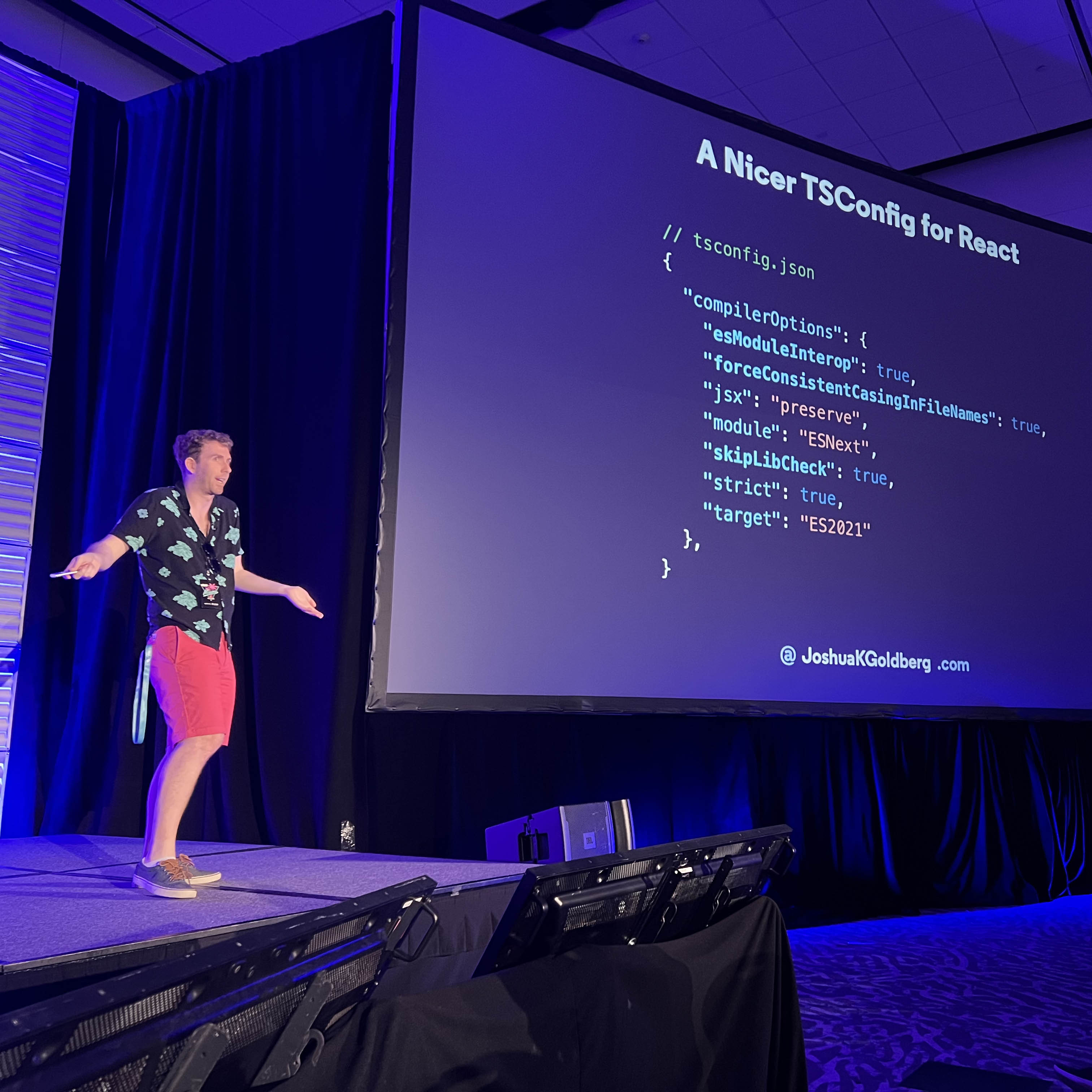 Josh smiling and gesturing on stage and giving a presentation showing the "Type Checking React (v2)" from the linked slides.